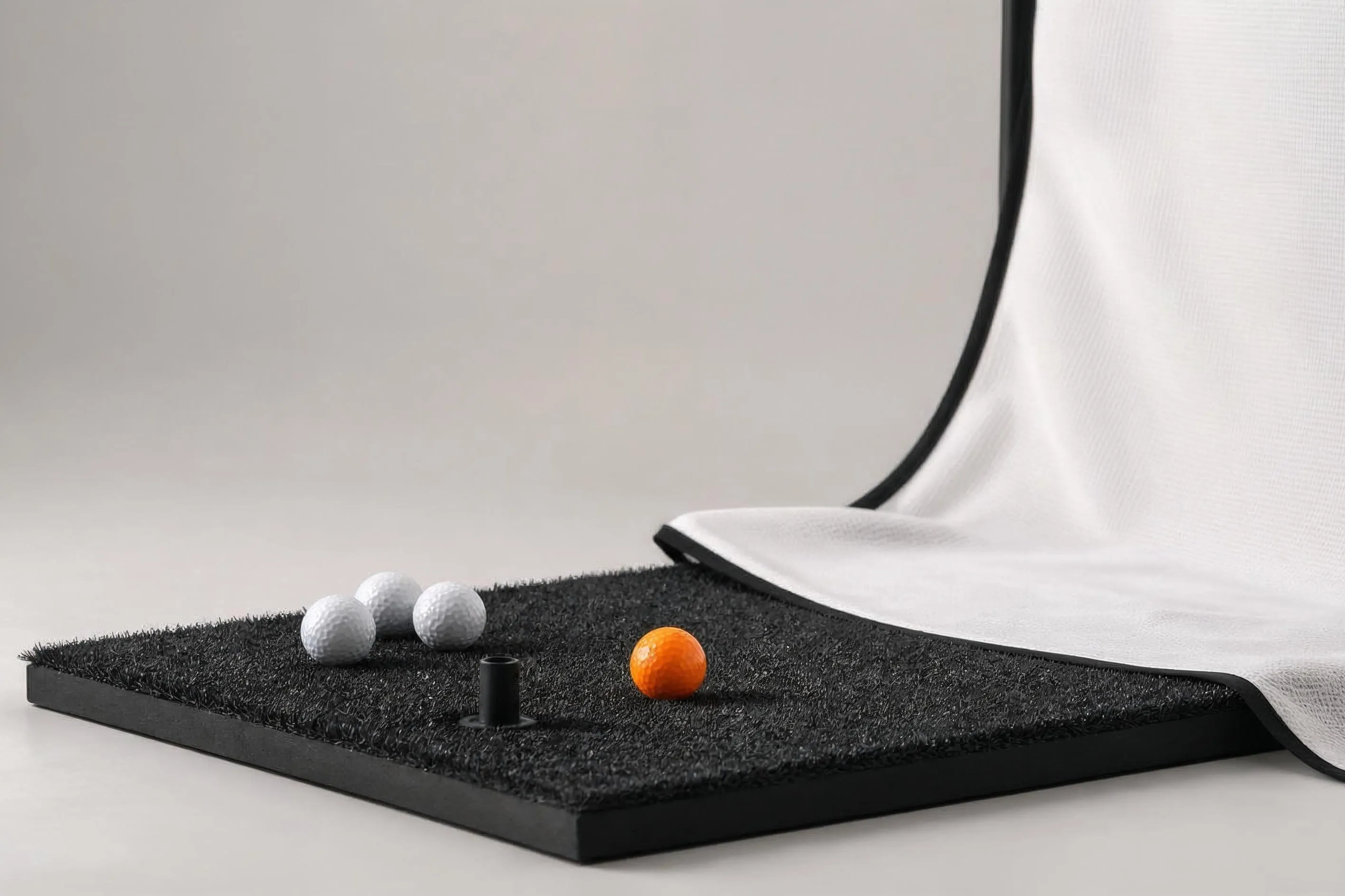Slagmatta med golfbollar och gummipegg framför en draperad impact screen i en hemmasimulator